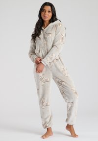 Grå fleece onesie med teddy-bjørn mønster, lynlås foran og hætte. Blødt materiale, manchetter ved håndled og ankler, med små hjerte detaljer overalt.