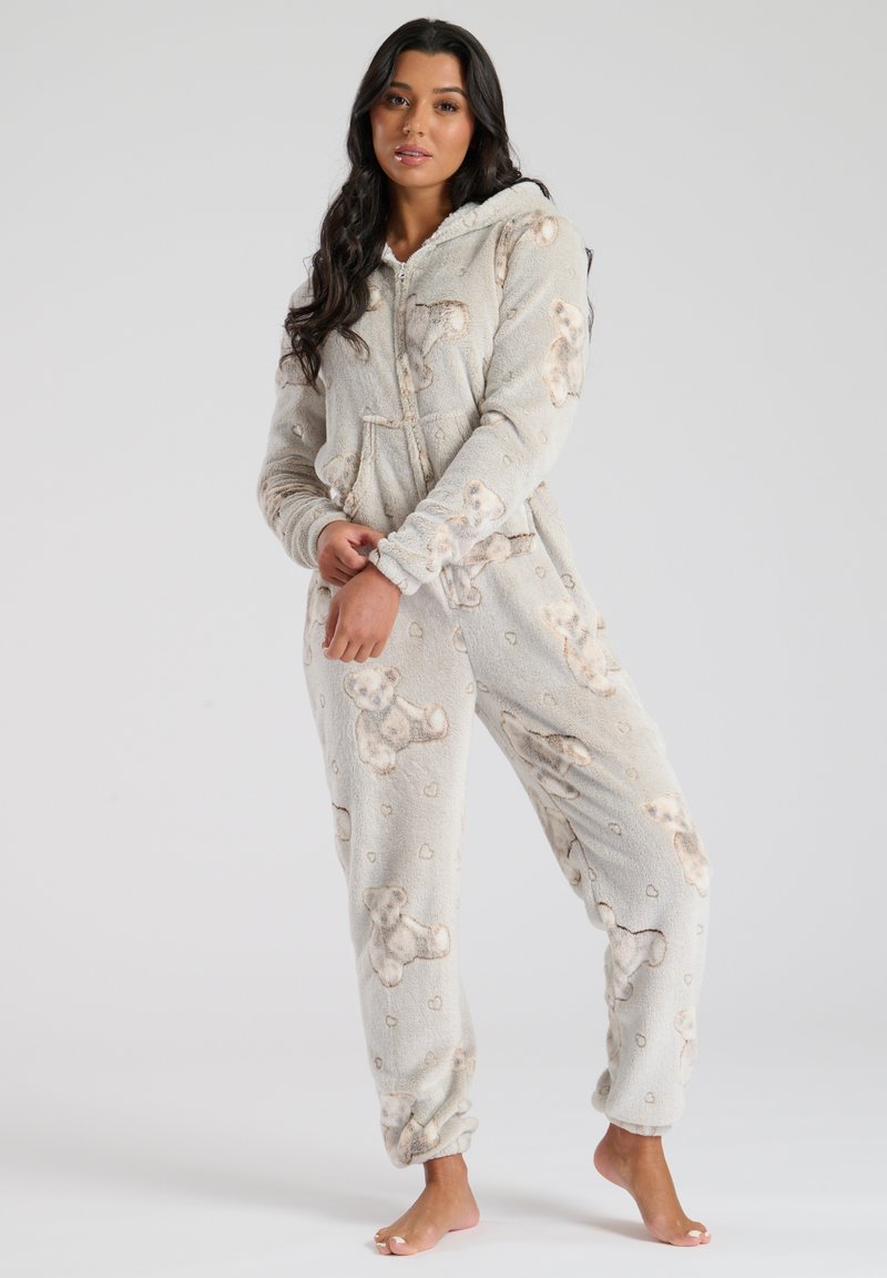 Grå fleece onesie med teddy-bjørn mønster, lynlås foran og hætte. Blødt materiale, manchetter ved håndled og ankler, med små hjerte detaljer overalt.