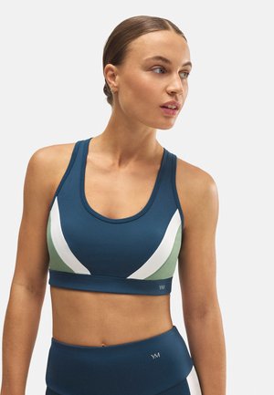 S sujetador deportivo de color azul oscuro con acentos diagonales en verde y blanco, que presenta un escote redondo y un diseño ajustado y sin costuras.