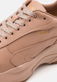 Ljust rosa lädersneaker med texturerade, vävda snörningar. Har en prägling av "BOSS"-logotypen i guld och en något upphöjd sula. Slät yta.