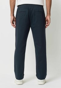 Námorně modré, lehké kalhoty s elastickým pasem, dvěma zadními kapsami a rovnými nohavicemi, doplněné bílými teniskami.