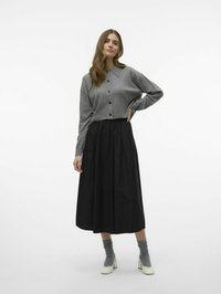Cardigan grigio in misto lana con colletto e bottoni, abbinato a una gonna midi plissettata nera. Vengono indossati calzini grigi e scarpe beige con tacco a blocco.