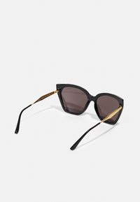 Lunettes de soleil en œil de chat avec des montures noires et des verres foncés. Éléments en métal doré sur les tempes. Design élégant avec une finition brillante.