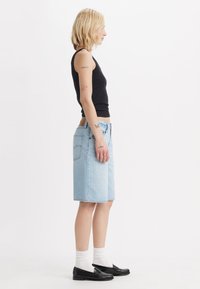 Svetlo modra jeans krilo do kolen s ravnim krojem, v kombinaciji z črno brezrokavnikom in črnimi loaferji, ki vključujejo bele nogavice.