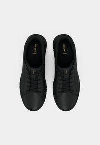 Μαύρα αθλητικά παπούτσια με λείο δερμάτινο επάνω μέρος, στρογγυλή μύτη και επίπεδα κορδόνια, με διακριτική σήμανση στη γλώσσα και την ύφασμα της σόλας.