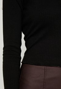 Svart ribbad långärmad topp med en kort design. Har ett strukturerat tyg och råa fållar. Kombinerad med en brun läderkjol.