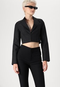 Blazer preto cropped com um design ajustado e mangas longas, combinado com calças pretas de cintura alta. Tecido liso e elegante com uma silhueta estruturada.