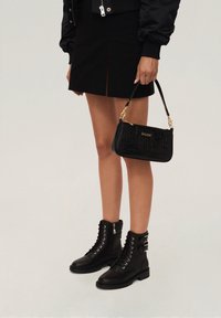 Black crocodile-patterned handbag with gold hardware, paired with black ankle boots featuring lace-up detail and buckles. Short black skirt visible.