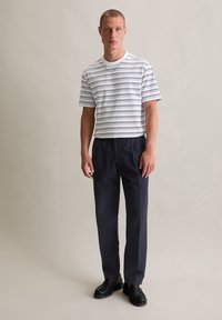 Gestreepte short-sleeve katoenen t-shirt in wit en marineblauw, gecombineerd met lichtgewicht donkerblauwe broeken. Model draagt zwarte loafers. Neutrale achtergrond.