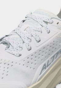 Λευκό αθλητικό παπούτσι με υφή, οπές για διαπνοή, κορδόνια με σχέδιο και το λογότυπο "ALTRA" στο μέσο της σόλας στο πλάι.