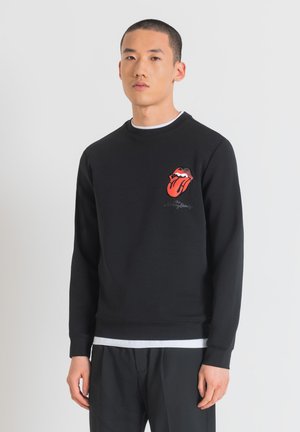 Sudadera negra de algodón con cuello redondo. Presenta un logotipo bordado de los Rolling Stones en rojo y negro en el pecho.