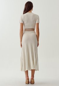 Krämfärgad ribbad stickad klänning med korta ärmar, prydd med vertikala beige ränder, en figurnära byst och en utsvängd kjol som faller under knäna.