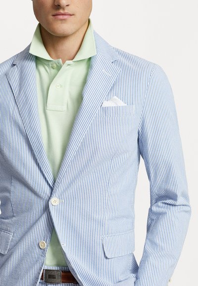 Blazer rayé bleu clair avec des rayures blanches, doté d'une fermeture à un bouton, de poches avant et d'un mouchoir blanc dans la poche poitrine.