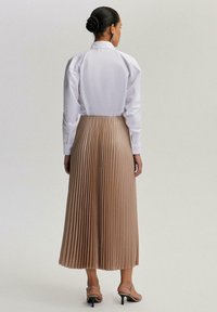 Valkoinen kauluspaita, beige pleated-hame, joka ulottuu polven keskelle, sileä tekstuuri ja avonainen selkädesign. Strappy-korkokengät viimeistelevät asun.