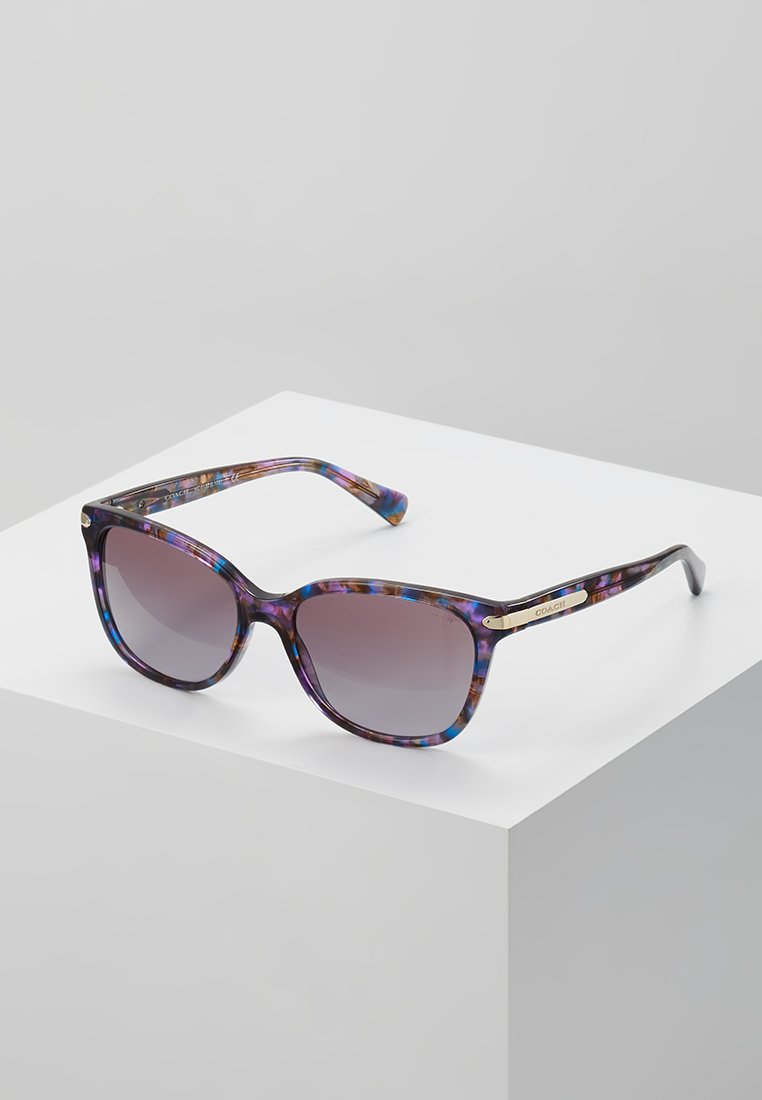 Ochelari de soare tortoiseshell în nuanțe de mov și albastru, cu lentile degradé și detalii din aur, având o formă ușor supradimensionată, tip cat-eye.