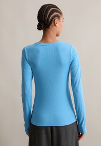 Lange mouwen, blauwe ribbeltop met een ronde halslijn, aansluitend ontwerp en een gladde textuur, gecombineerd met een donkergrijze rok.