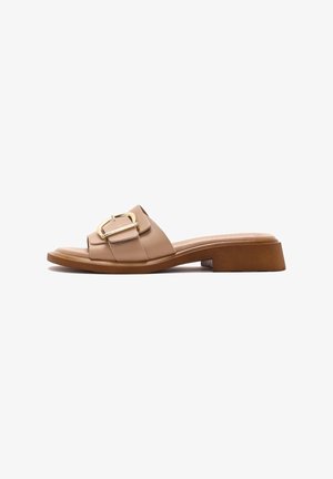 Des sandales à glisser en cuir beige présentent une large sangle avec une boucle dorée, une semelle plate et un design de talon bas et épais.