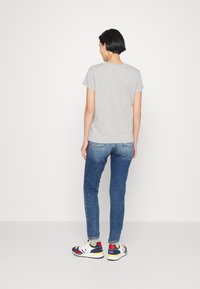 Camiseta gris de manga corta, combinada con vaqueros azules y zapatillas multicolores. Diseño sencillo, enfoque en la moda casual.