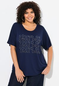 Námořnická modrá oversized tričko s krátkým rukávem, s opakovaným stříbrným textovým designem "SOUND OF JUNGLE DRUM." Hladká textura látky.