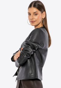 Black leather jacket with a fitted design, long sleeves, and zippered details. Features a smooth texture and minimalistic style.