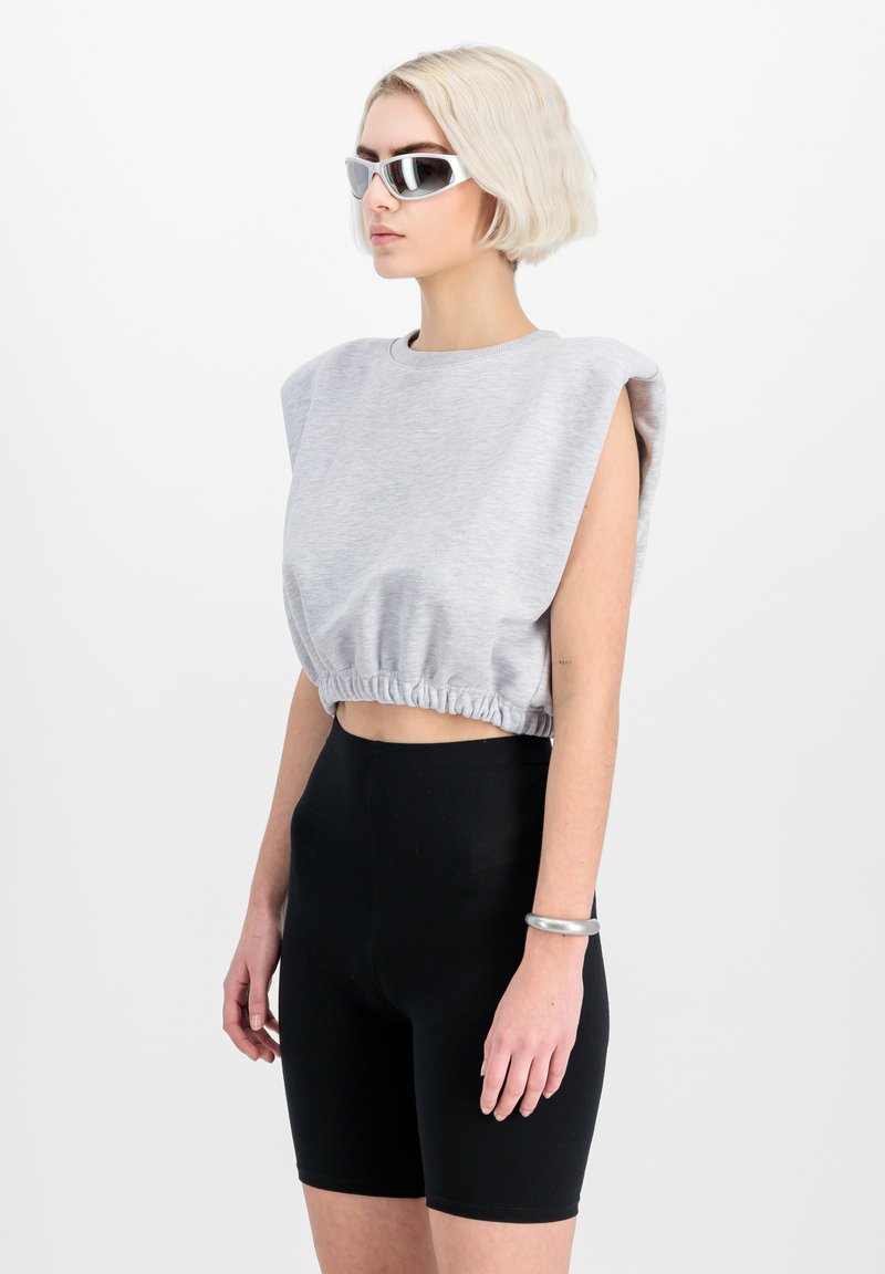 Felpa grigia corta con design a spalle larghe, orlo elastico e maniche corte, abbinata a pantaloni da ciclismo neri aderenti. Occhiali da sole argentati e bracciale.