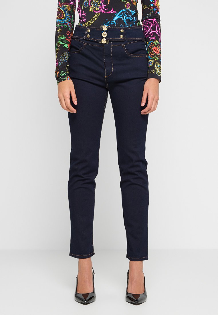 Granatowe, wysokie dżinsy z pięcioma złotymi guzikami, kontrastowym przeszyciem i dopasowanym krojem. Materiał wydaje się gładki z lekkim streczem.