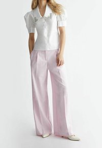 Weiße Bluse mit Puffärmeln und Strassakzent am Kragen, kombiniert mit rosa weit geschnittenen Hosen aus einem strukturierten Stoff.