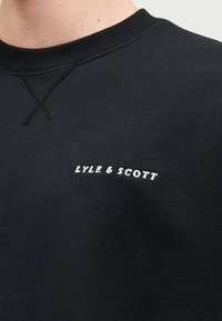 Μαύρο φούτερ από βαμβάκι, με ριμπ κολάρο και λευκό κεντημένο λογότυπο "LYLE & SCOTT" στην αριστερή πλευρά του στήθους.