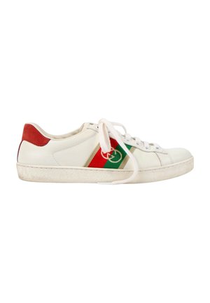 Biały niski sneaker z czerwoną piętą, zielono-czerwoną paską z logo po boku, białymi sznurówkami i lekko zużytą podeszwą.