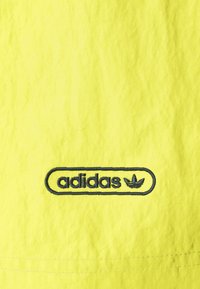 Bright yellow fabric with a crinkled texture featuring an embroidered Adidas logo in dark blue, including the iconic trefoil design.