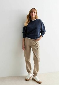Felpa navale, pantaloni cargo beige con tasche laterali e sneakers bianche con dettagli color cuoio. Vestibilità rilassata con polsini e vita a costine.