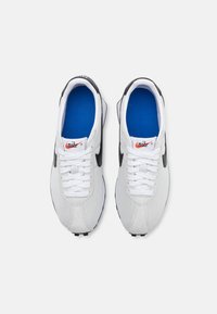 Bijele atletske tenisice s gornjim dijelom od mreže i antilopa, crnim detaljima i plavim ulošcima. Sadrže bijele vezice i Nike logo na jeziku.