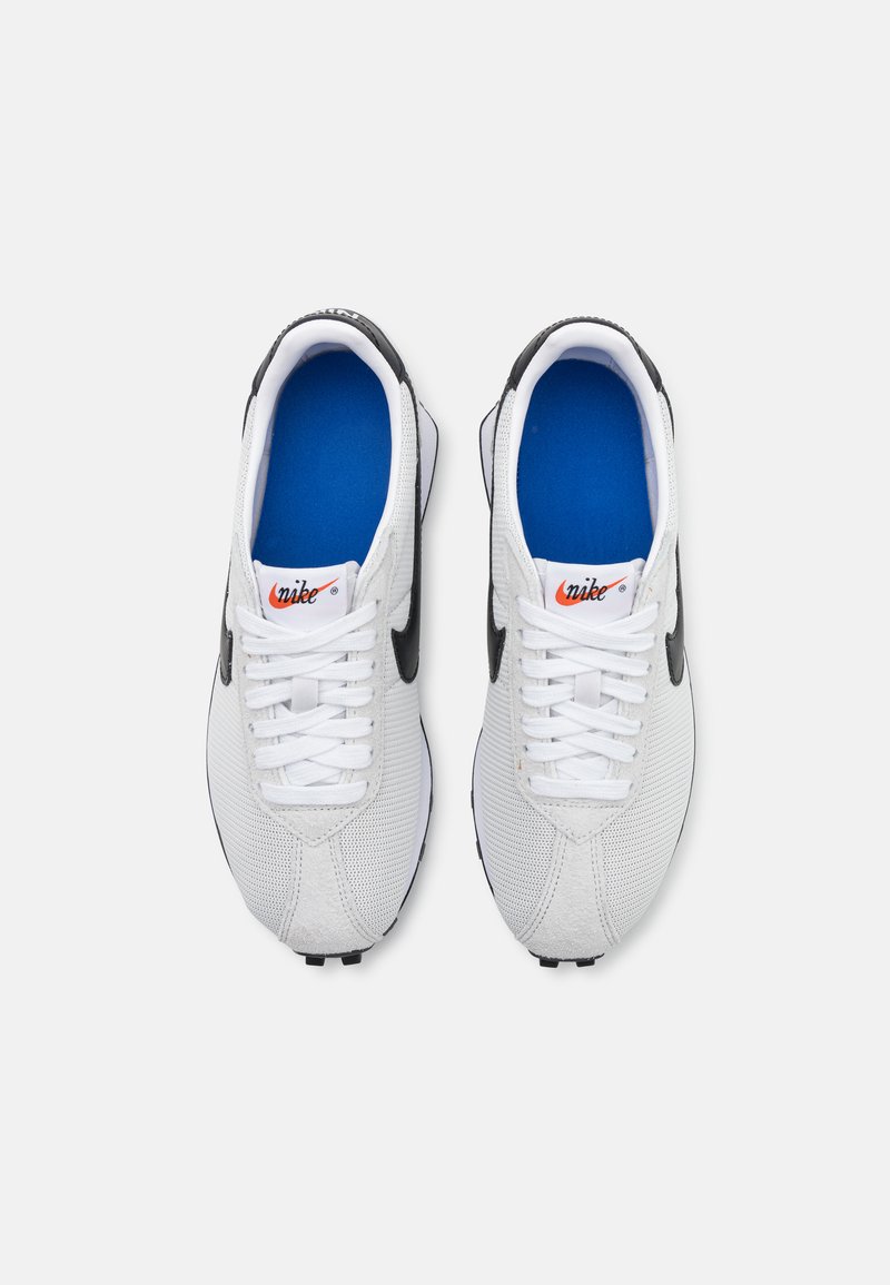 Zapatillas deportivas blancas con parte superior de malla y ante, acentos negros y plantillas azules. Presenta cordones blancos y el logo de Nike en la lengüeta.