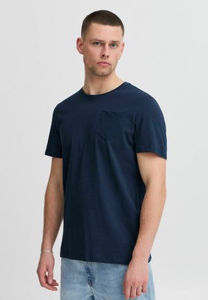 Marineblå bomulds T-shirt med korte ærmer, rund hals og en foret taske. Glat tekstur, afslappet pasform, parret med lyseblå jeans.