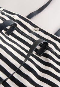 Borsa a righe bianche e nere con manici in pelle nera e chiusura a scatto magnetica su sfondo chiaro.