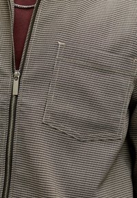 Schwarz-weiß karierte Zip-up-Jacke mit kleinem Brusttasche, kontrastierendem Reißverschluss und strukturiertem gewebtem Stoff.