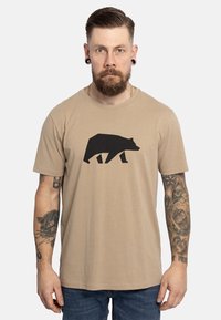 Camiseta de algodón color canela con un gráfico de oso geométrico negro en el frente. Cuello redondo, mangas cortas y un corte relajado.