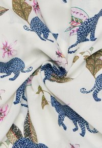 Katoenen stof met een witte achtergrond, featuring blauwe leopards en botanische patronen in roze en groene tinten. Gelaagd en levendig.