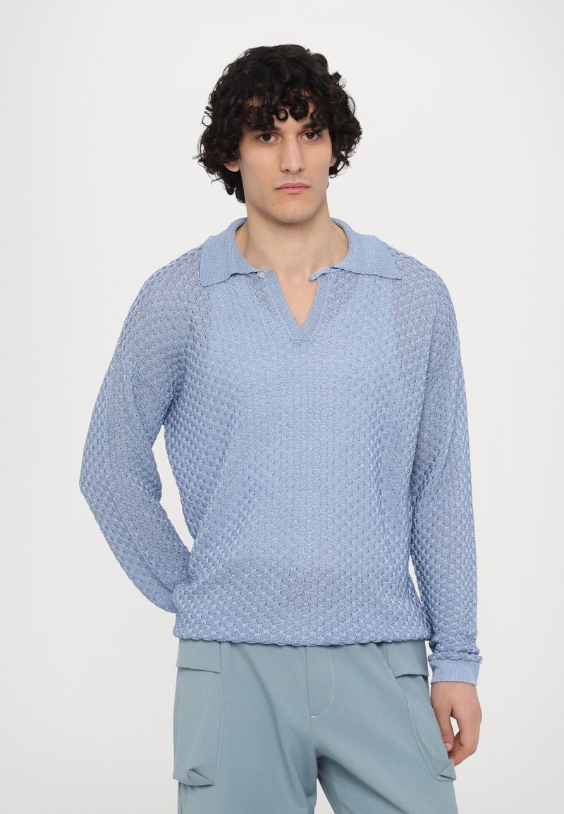 Pullover a maglia blu chiaro con un motivo a diamante testurizzato, colletto e maniche lunghe. Indossato con pantaloni di colore chiaro.