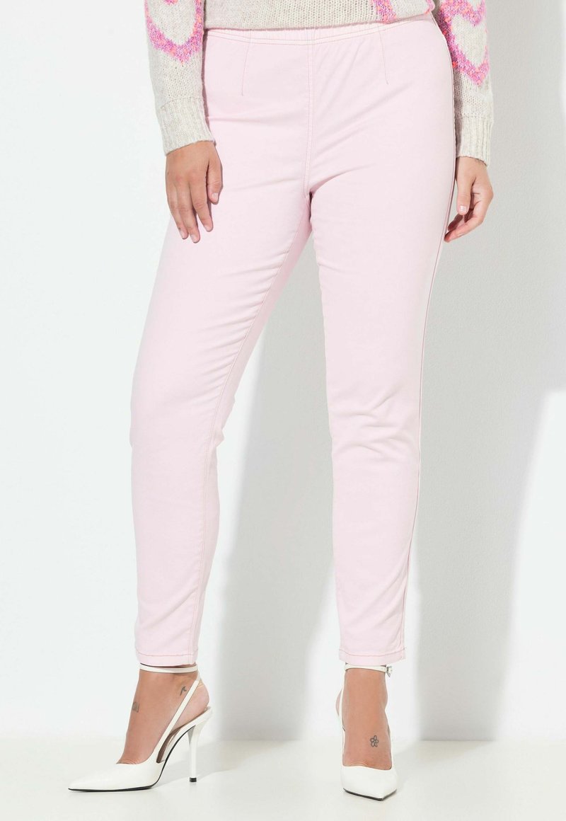 Vaaleanpunaiset istuvat housut, joissa on sileä pinta, joustava vyötärönauha ja kapeutuvat lahkeet. Yhdistetty valkoisiin piikkikorkoihin.