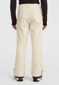 Lichtbeige skibroek met een losse pasvorm, elastische tailleband en laarzenbeschermers bij de enkels, gemaakt van waterafstotend materiaal.