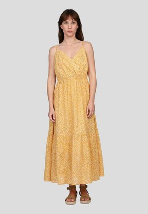 Robe maxi florale jaune avec un décolleté en V, des bretelles réglables, une taille élastique et un design de jupe superposée. Portée avec des sandales marron.