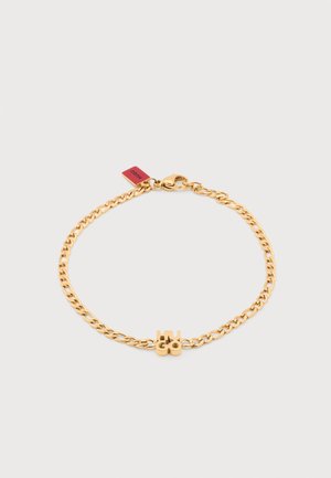 Zlatna narukvica s lancem s privjeskom u obliku slova "HUGO" i kopčom na karabin, s malom crvenom oznakom blizu kopče.