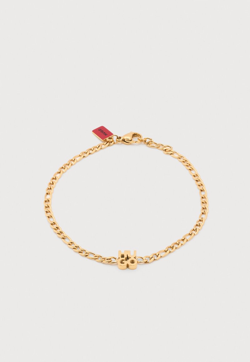 Βραχιόλι με χρυσή αλυσίδα, με κρεμαστό κόσμημα γράμματα "HUGO" και κούμπωμα αστακού, με μια μικρή κόκκινη ετικέτα κοντά στο κούμπωμα.