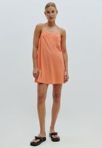 Orangenes, ärmelloses Kleid mit lockerer Passform, aus leichtem Stoff, mit geradem Saum und schmalen Trägern. Getragen mit schwarzen Plateau-Sandalen.