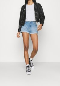 Svart läderjacka, grå T-shirt, ljusblå upprullade denimshorts och svarta högst sportskor. Enkelt mönster med avslappnad passform.