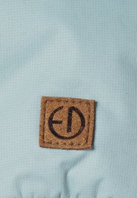 Ljusblått tyg med en brun fyrkantig lappar med en svart logotyp och sömdetaljer. Texturen är slät med ett vävt mönster.