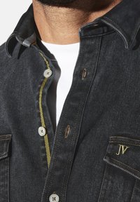 Dunkelblaue Jeanshemd mit gelben Nähten, ausgestattet mit einer Knopfleiste, zwei Brusttaschen und gestickten Initialen "JV" auf der Tasche.