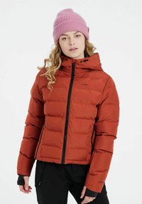 Rød isoleret jakke med polstret design, sort lynlås og hætte; båret med sorte bukser. Modellen bærer også en lyserød strikket beanie.
