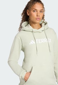 Jasnozielona bluza z kapturem z dużym białym logo "TERREX", regulowanym kapturem na sznurki oraz przednią kieszenią typu kangur. Wykonana z bawełny.